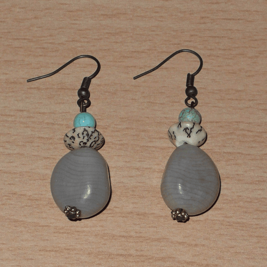 Boucles d'oreilles exotiques composées de perles et de graines de caniques grises. De taille moyenne, elles mesurent 5 cm de long et 1,5 cm de large, et se portent sur des oreilles percées.