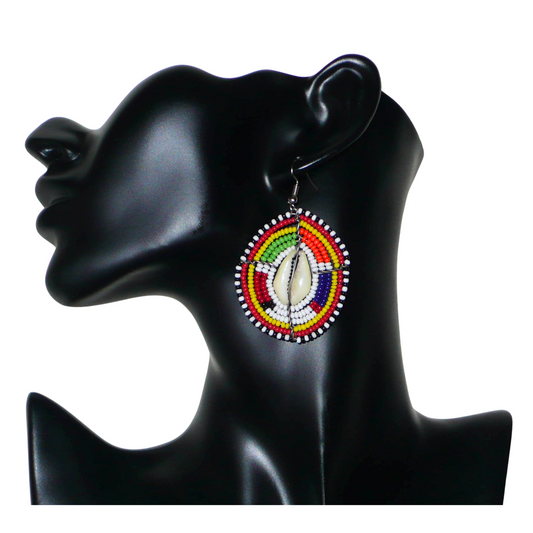 Ambiance traditionnelle Massai avec ce modèle de boucles d'oreilles africaines aux couleurs exotiques et motifs ethniques ! De fabrication tribale artisanale kenyane, elles sont composées de perles de rocaille blanches et multicolores et de coquillages fixés sur des fils de fer montés en forme de boucliers Massai. Ces boucles d'oreilles de taille moyenne mesurent 6.5 cm de long et 4 cm de large, et se portent avec des crochets en acier inoxydable sur des oreilles percées.