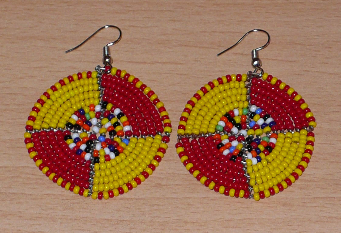 Boucles d'oreilles exotiques ultra colorées en perles de rocaille rouges, jaunes et multicolores montées en forme de disques. Elles mesurent 6 cm de long et 4 cm de large et se portent sur des oreilles percées.