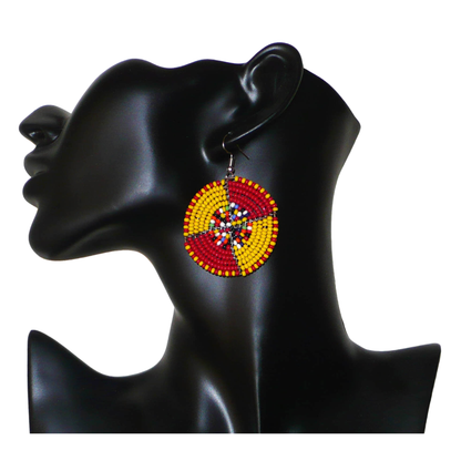 Boucles d'oreilles exotiques ultra colorées en perles de rocaille rouges, jaunes et multicolores montées en forme de disques. Elles mesurent 6 cm de long et 4 cm de large et se portent sur des oreilles percées.