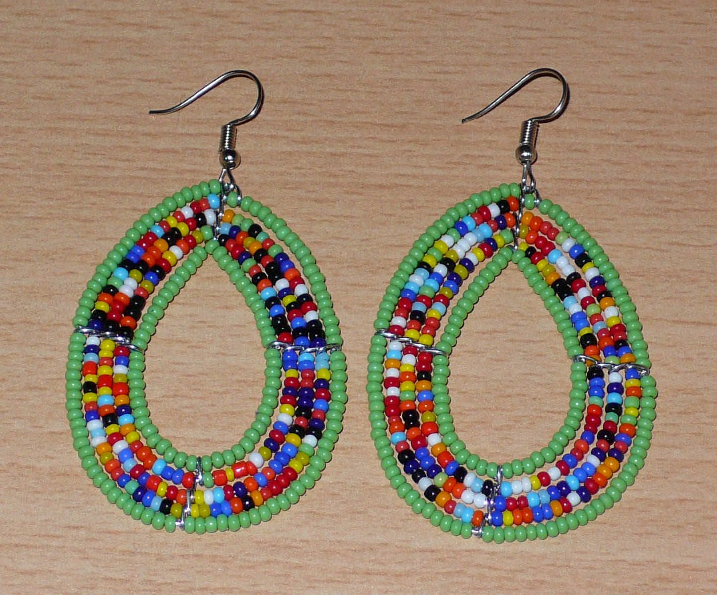 Boucles d'oreilles exotiques vertes et multicolores en forme de gouttes. Elles mesurent 7.5 cm de long et 4 cm de large et se portent sur des oreilles percées.