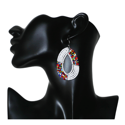 Boucles d'oreilles kenyanes multi-rangs en forme de gouttes composées de perles de rocaille blanches et multicolores. De taille moyenne, elles mesurent 7 cm de long et 4 cm de large, et se portent sur des oreilles percées.