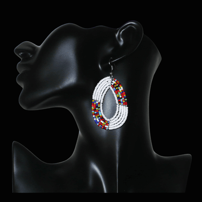 Boucles d'oreilles kenyanes multi-rangs en forme de gouttes composées de perles de rocaille blanches et multicolores. De taille moyenne, elles mesurent 7 cm de long et 4 cm de large, et se portent sur des oreilles percées.