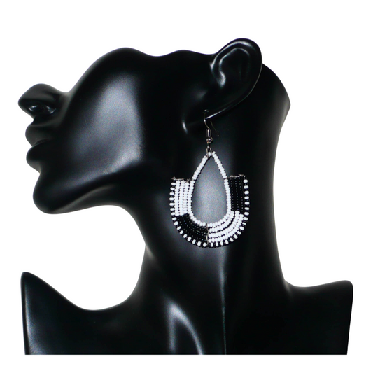 Ajoutez une touche ethnique contemporaine à votre tenue avec cette paire de boucles d'oreilles africaines bicolores blanches et noires ! De fabrication artisanale kenyane, elles se composent de perles de rocaille blanches et noires glissées sur des structures en fils de fer montés en forme d'ancres. Ces boucles d'oreilles mesurent 7 cm de long et 4 cm de large, et se portent avec des crochets en acier inoxydable sur des oreilles percées.