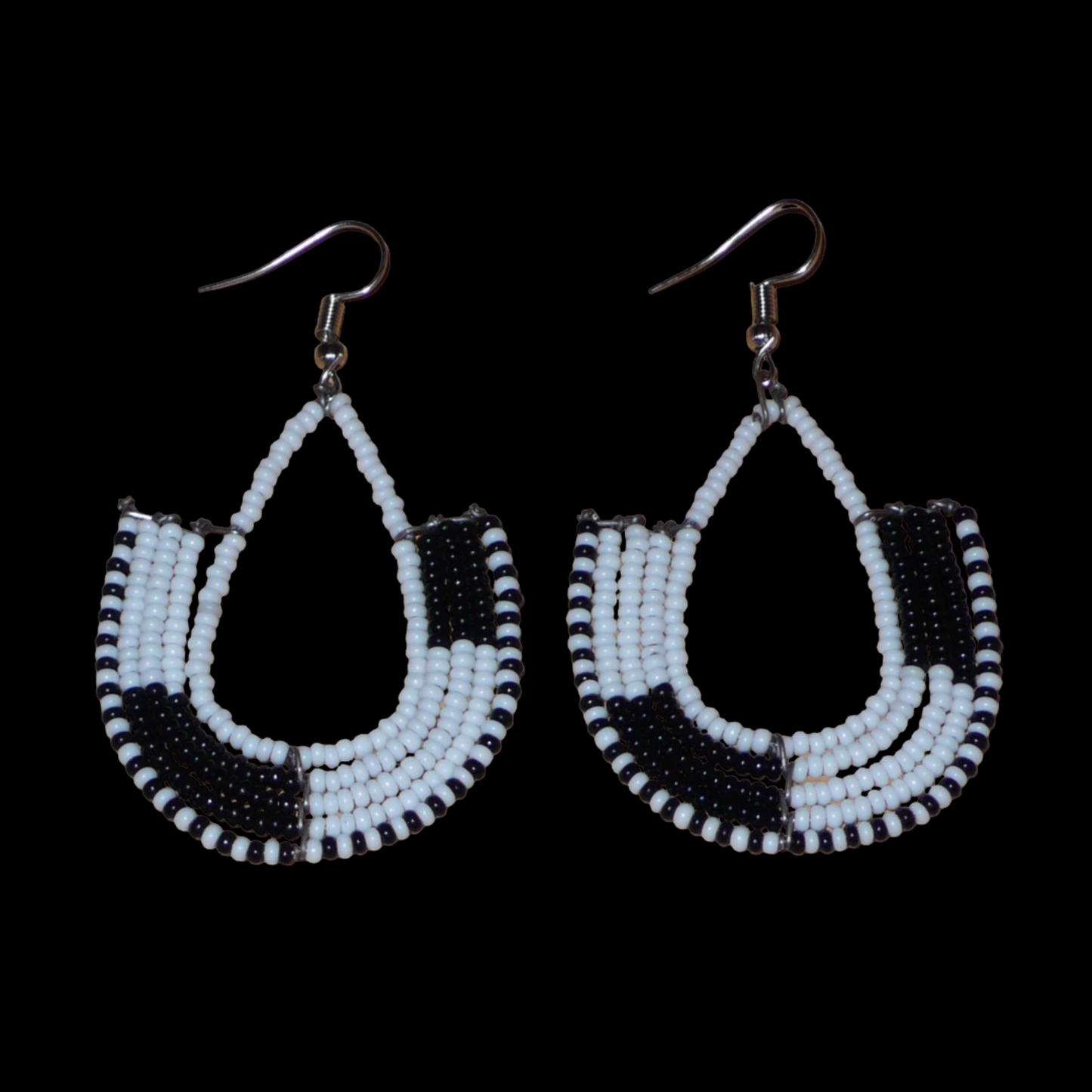 Ajoutez une touche ethnique contemporaine à votre tenue avec cette paire de boucles d'oreilles africaines bicolores blanches et noires ! De fabrication artisanale kenyane, elles se composent de perles de rocaille blanches et noires glissées sur des structures en fils de fer montés en forme d'ancres. Ces boucles d'oreilles mesurent 7 cm de long et 4 cm de large, et se portent avec des crochets en acier inoxydable sur des oreilles percées.