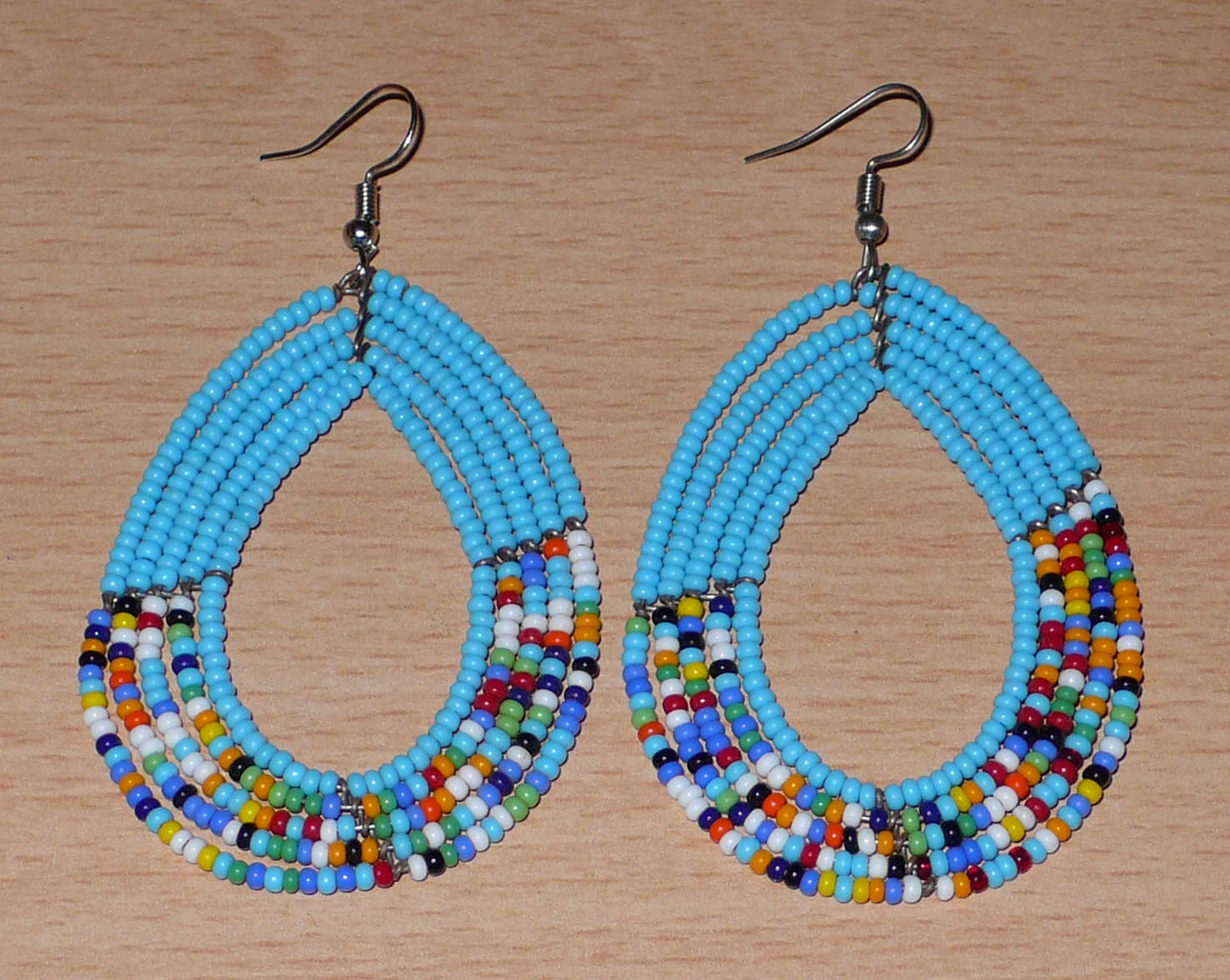Boucles d'oreilles kenyanes en perles de rocaille bleu ciel et multicolores montées en forme de gouttes. Elles mesurent 8 cm de long et 4.5 cm de large, et se portent sur des oreilles percées.