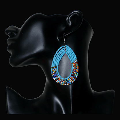 Boucles d'oreilles kenyanes en perles de rocaille bleu ciel et multicolores montées en forme de gouttes. Elles mesurent 8 cm de long et 4.5 cm de large, et se portent sur des oreilles percées.