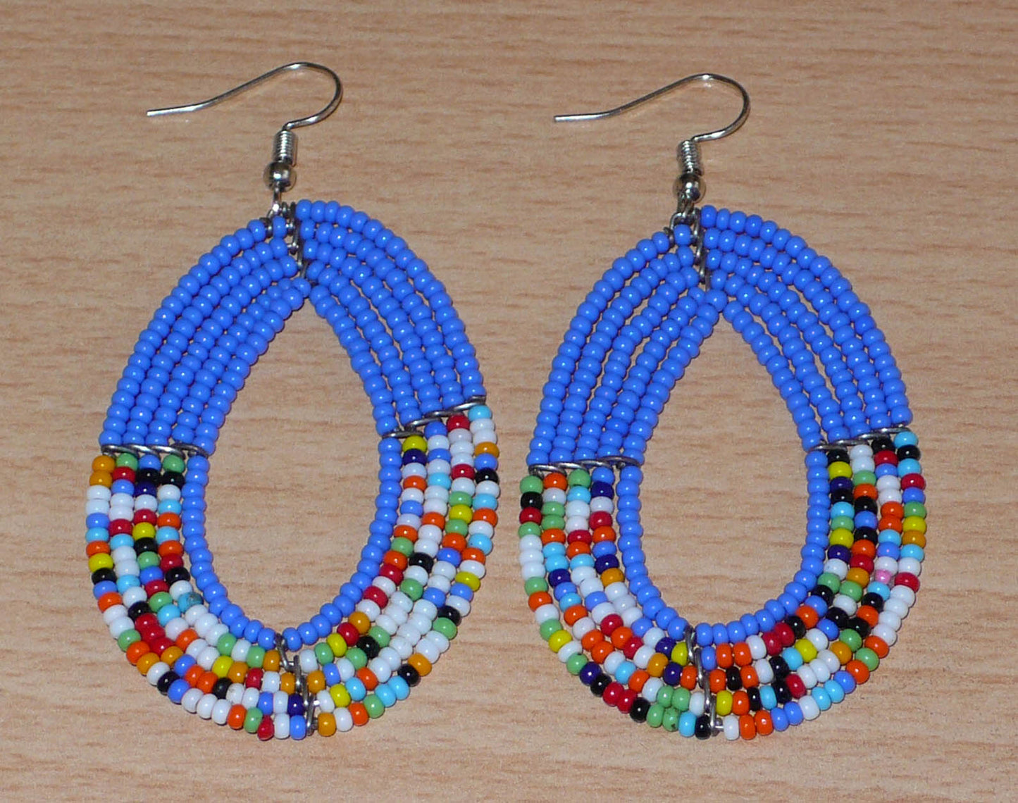 Boucles d'oreilles kenyanes multi-rangs de forme ovales, en perles de rocaille bleues et multicolores. Elles mesurent 7.5 cm de long et 4 cm de large et se portent sur des oreilles percées.