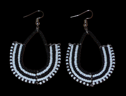 Boucles d'oreilles kenyanes Massai bicolores en forme d'ancres composées de perles de rocaille noires et blanches glissées sur des structures géométriques en fils de fer. De taille moyenne, ces boucles d'oreilles aux accents ethniques afro chic mesurent 7 cm de long et 4 cm de large ; elles se portent avec des crochets en acier inoxydable sur des oreilles percées.