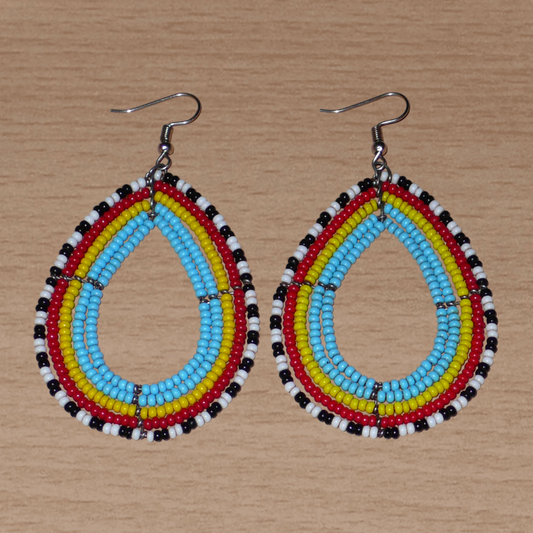 Boucles d'oreilles kenyanes Massai tricolores aux contours noirs et blancs composées de perles de rocaille montées en forme de gouttes. Elles mesurent 8 cm de long et 4.5 cm de large, et se portent sur des oreilles percées.
