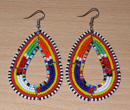 Ajoutez de la couleur à votre look avec ces longues boucles d'oreilles africaines à motifs ethniques traditionnels Massai. Confectionnées selon la tradition artisanale kenyane, elles sont composées de perles de rocaille multicolores glissées sur six rangées de fils de fer montés en forme de gouttes. Ces boucles d'oreilles mesurent 8 cm de long et 4.5 cm de large ; elles se portent avec des crochets en acier inoxydable sur des oreilles percées.