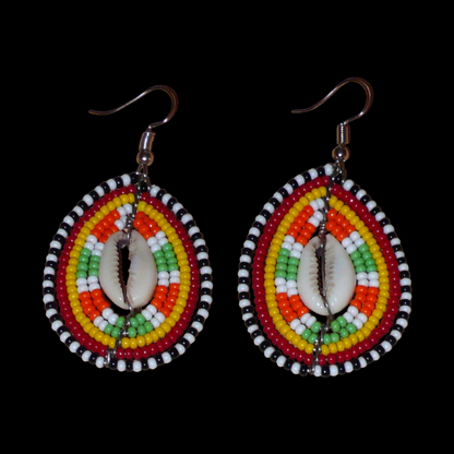 Boucles d'oreilles kenyanes à motifs ethniques en forme de boucliers Massai ; elles se composent de perles et de coquillages cauris, et mesurent 7 cm de long et 4 cm de large, elles se portent sur des oreilles percées.