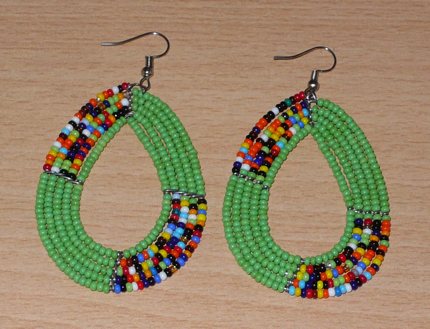 Boucles d'oreilles kenyanes vertes et multicolores en perles de rocaille enfilées sur cinq rangées de fils de fer montés en forme de gouttes. Elles mesurent 8 cm de long et 4.5 cm de large, et se portent sur des oreilles percées.