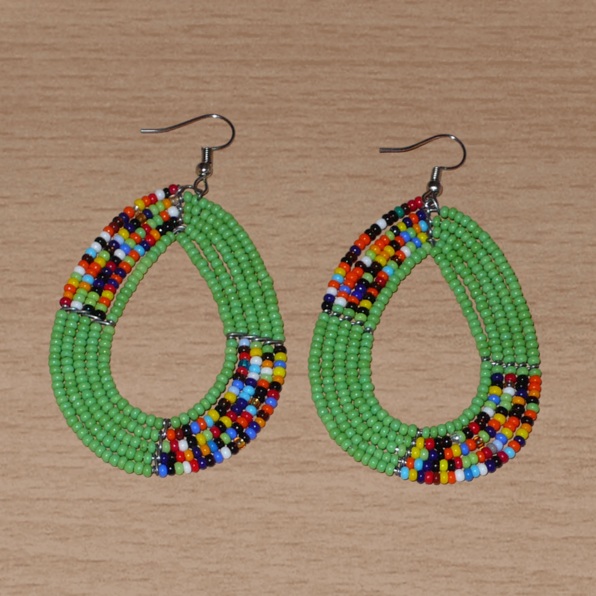 Boucles d'oreilles kenyanes vertes et multicolores en perles de rocaille enfilées sur cinq rangées de fils de fer montés en forme de gouttes. Elles mesurent 8 cm de long et 4.5 cm de large, et se portent sur des oreilles percées.