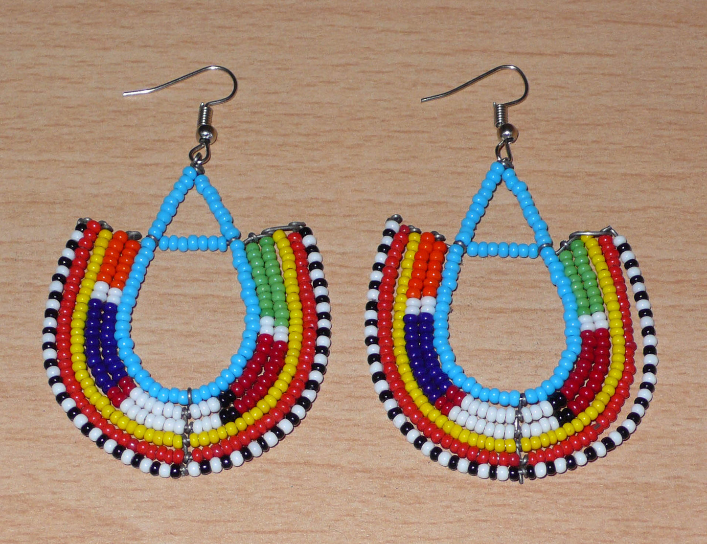 Cette paire de boucles d'oreilles africaines traditionnelles Massai en forme d'ancres, de conception artisanale kenyane, apportera une touche ethnique à votre look ! D'allure exotique et riches en couleurs, elles se composent de perles de rocaille bleues et multicolores glissées sur des structures géométriques en fils de fer montés en forme d'ancres. Ces boucles d'oreilles mesurent 7.5 cm de long et 4.5 cm de large, et se portent avec des crochets en acier inoxydable sur des oreilles percées.