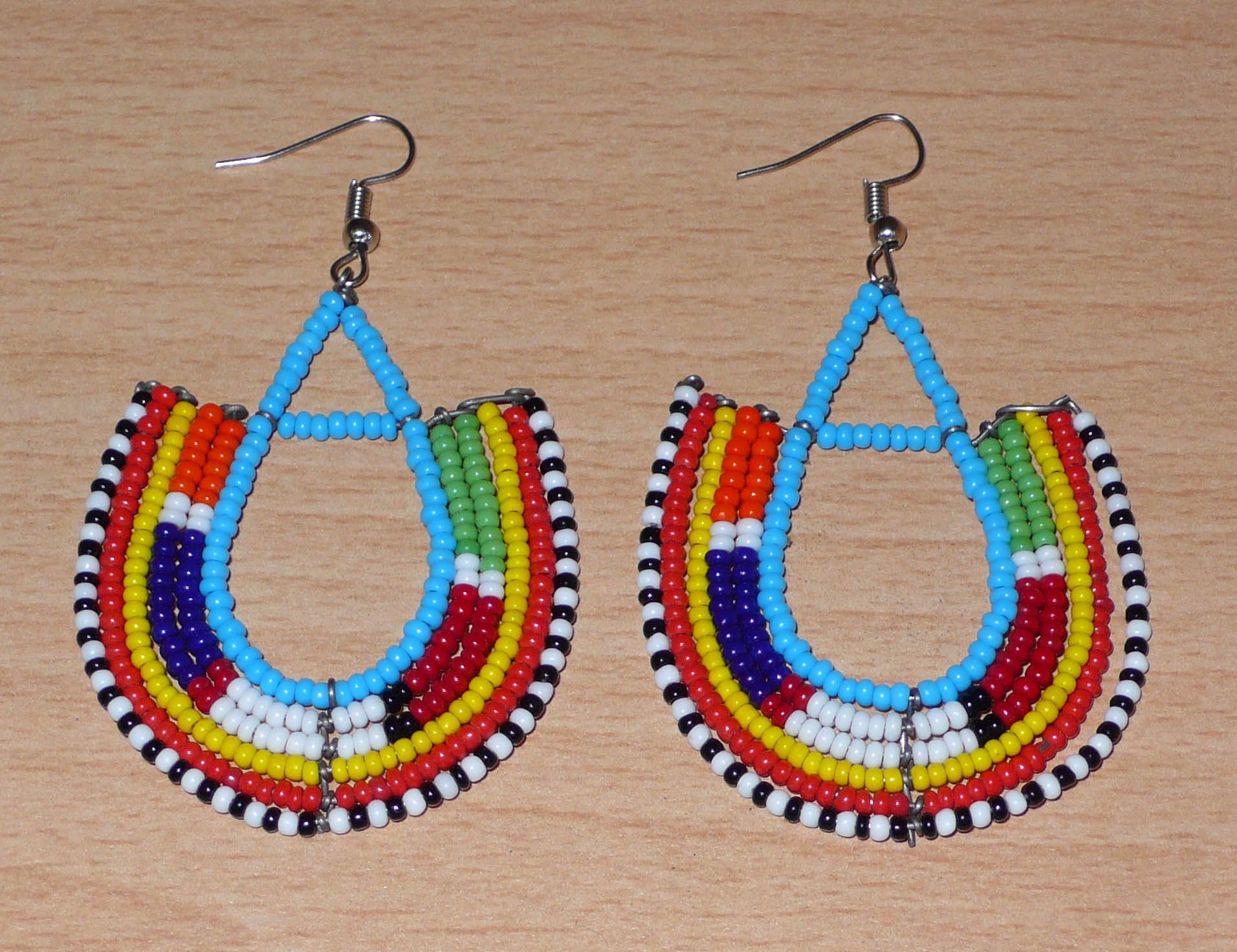 Cette paire de boucles d'oreilles africaines traditionnelles Massai en forme d'ancres, de conception artisanale kenyane, apportera une touche ethnique à votre look ! D'allure exotique et riches en couleurs, elles se composent de perles de rocaille bleues et multicolores glissées sur des structures géométriques en fils de fer montés en forme d'ancres. Ces boucles d'oreilles mesurent 7.5 cm de long et 4.5 cm de large, et se portent avec des crochets en acier inoxydable sur des oreilles percées.