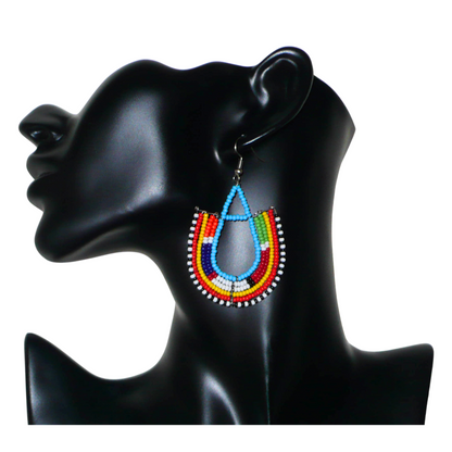 Cette paire de boucles d'oreilles africaines traditionnelles Massai en forme d'ancres, de conception artisanale kenyane, apportera une touche ethnique à votre look ! D'allure exotique et riches en couleurs, elles se composent de perles de rocaille bleues et multicolores glissées sur des structures géométriques en fils de fer montés en forme d'ancres. Ces boucles d'oreilles mesurent 7.5 cm de long et 4.5 cm de large, et se portent avec des crochets en acier inoxydable sur des oreilles percées.