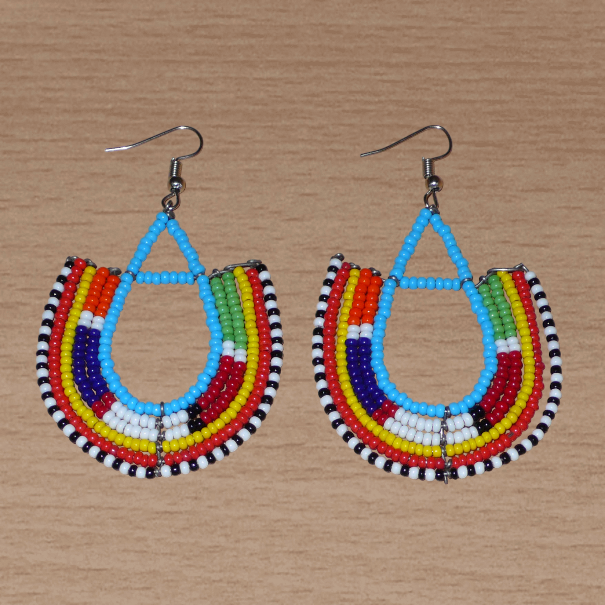 Cette paire de boucles d'oreilles africaines traditionnelles Massai en forme d'ancres, de conception artisanale kenyane, apportera une touche ethnique à votre look ! D'allure exotique et riches en couleurs, elles se composent de perles de rocaille bleues et multicolores glissées sur des structures géométriques en fils de fer montés en forme d'ancres. Ces boucles d'oreilles mesurent 7.5 cm de long et 4.5 cm de large, et se portent avec des crochets en acier inoxydable sur des oreilles percées.
