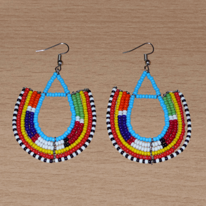 Cette paire de boucles d'oreilles africaines traditionnelles Massai en forme d'ancres, de conception artisanale kenyane, apportera une touche ethnique à votre look ! D'allure exotique et riches en couleurs, elles se composent de perles de rocaille bleues et multicolores glissées sur des structures géométriques en fils de fer montés en forme d'ancres. Ces boucles d'oreilles mesurent 7.5 cm de long et 4.5 cm de large, et se portent avec des crochets en acier inoxydable sur des oreilles percées.