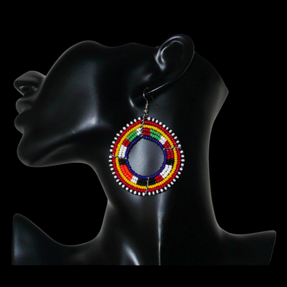 Boucles d'oreilles africaines rondes à motifs ethniques Massai faites de perles bleu foncé et multicolores. Elles mesurent 7 cm de long et 5 cm de large et se portent avec des crochets en acier inoxydable sur des oreilles percées.