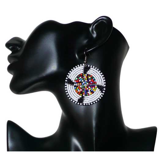 Ajoutez une touche ethnique à votre style avec ces boucles d'oreilles africaines rondes confectionnées dans la tradition artisanale Massai. Elles se composent de perles de rocaille principalement blanches, puis noires et multicolores glissées sur des structures circulaires en fils de fer. Cette paire de boucles d'oreilles mesure 6.5 cm de long et 4.5 cm de large, et se porte avec des crochets en acier inoxydable sur des oreilles percées.