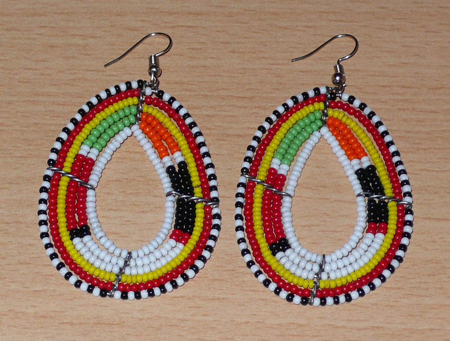 Boucles d'oreilles Massai multi-rangs blanches et multicolores faites de perles de rocaille montées en forme de gouttes. Elles mesurent 7. cm de long et 4 cm de large, et se portent sur des oreilles percées.