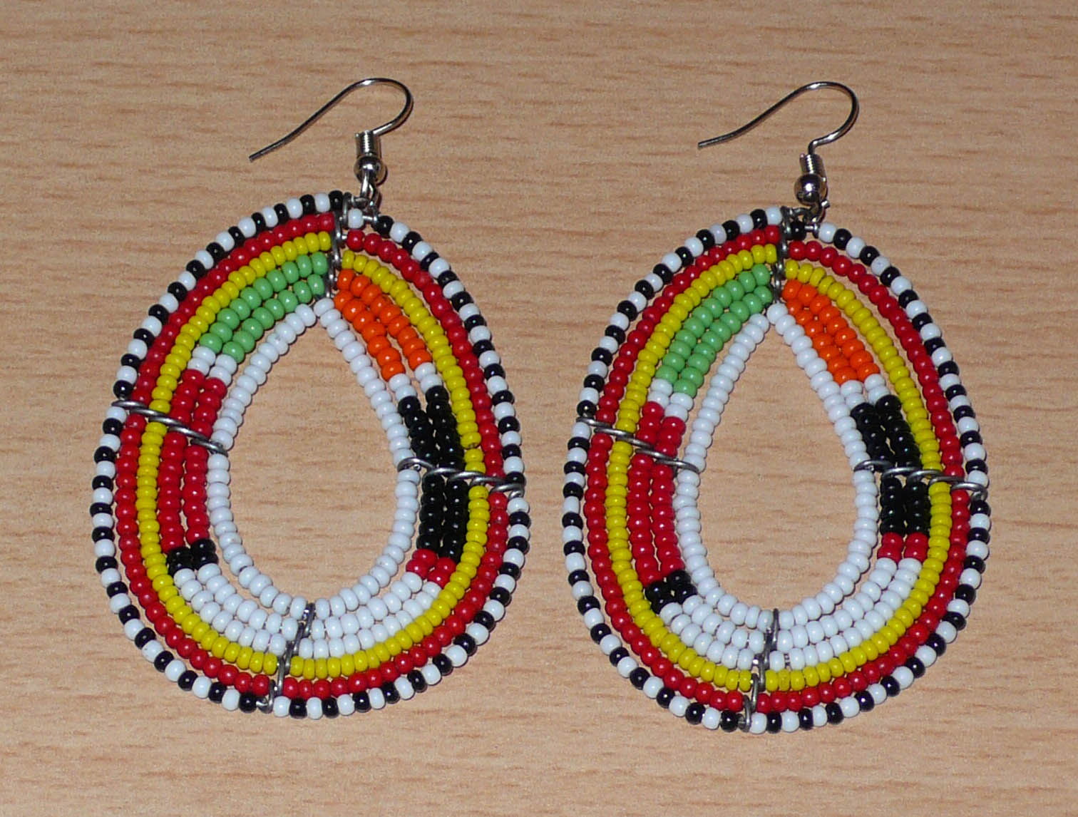 Boucles d'oreilles Massai multi-rangs blanches et multicolores faites de perles de rocaille montées en forme de gouttes. Elles mesurent 7. cm de long et 4 cm de large, et se portent sur des oreilles percées.