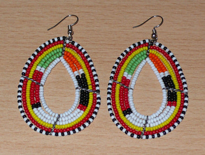 Boucles d'oreilles Massai multi-rangs blanches et multicolores faites de perles de rocaille montées en forme de gouttes. Elles mesurent 7. cm de long et 4 cm de large, et se portent sur des oreilles percées.