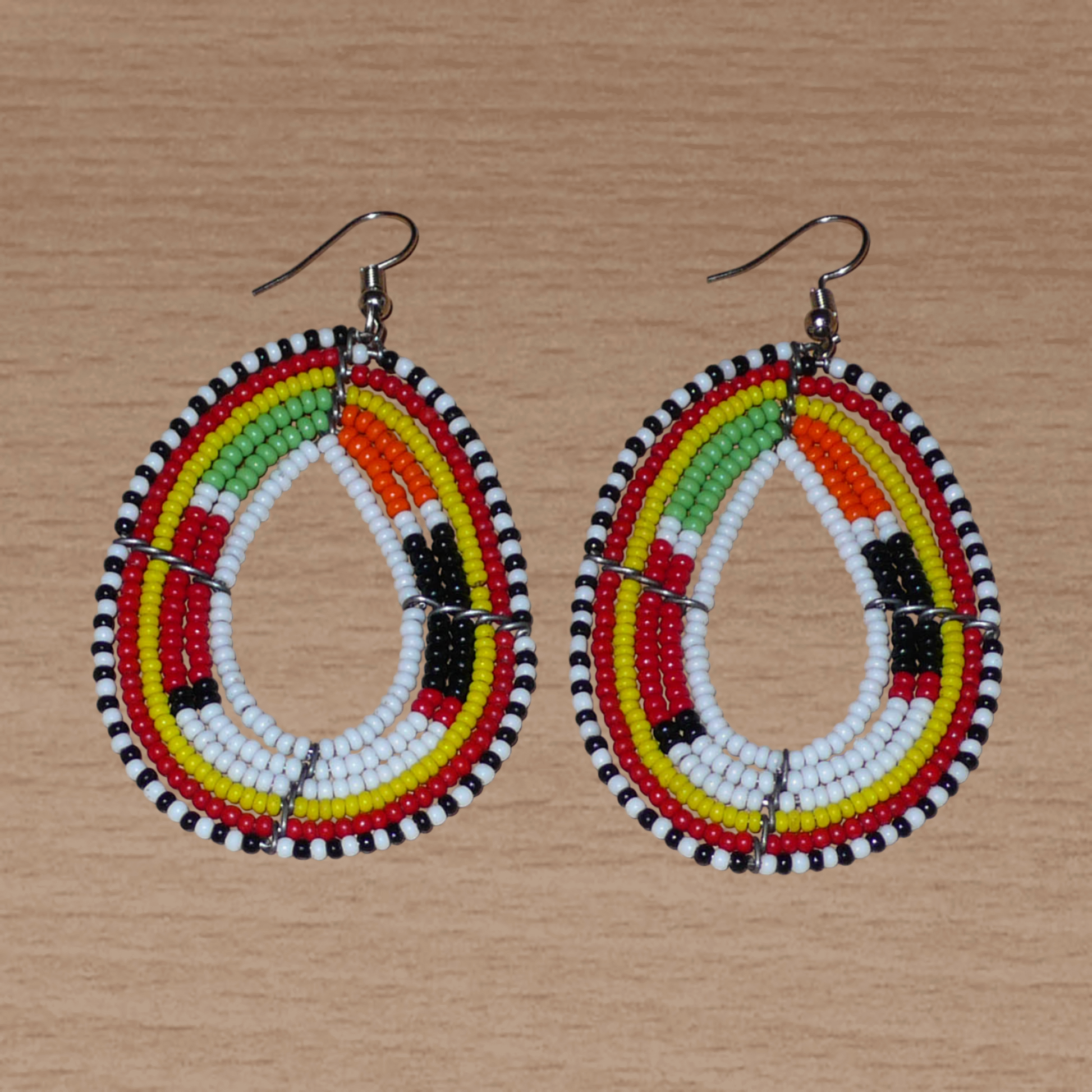 Boucles d'oreilles Massai multi-rangs blanches et multicolores faites de perles de rocaille montées en forme de gouttes. Elles mesurent 7. cm de long et 4 cm de large, et se portent sur des oreilles percées.