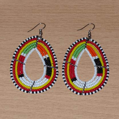 Boucles d'oreilles Massai multi-rangs blanches et multicolores faites de perles de rocaille montées en forme de gouttes. Elles mesurent 7. cm de long et 4 cm de large, et se portent sur des oreilles percées.