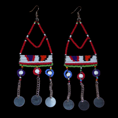 Ajoutez une touche ethnique à votre look avec ces superbes boucles d'oreilles africaines Massai rouges et multicolores fabriquées dans la plus pure tradition artisanale kenyane. Elles se composent de perles de rocaille rouges et multicolores et de perles en plastique enfilées sur des structures à formes géométriques en fils de fer, et se prolongent de chaînettes décorées de disques métalliques. Surdimensionnées, elles mesurent 15.5 cm de long.