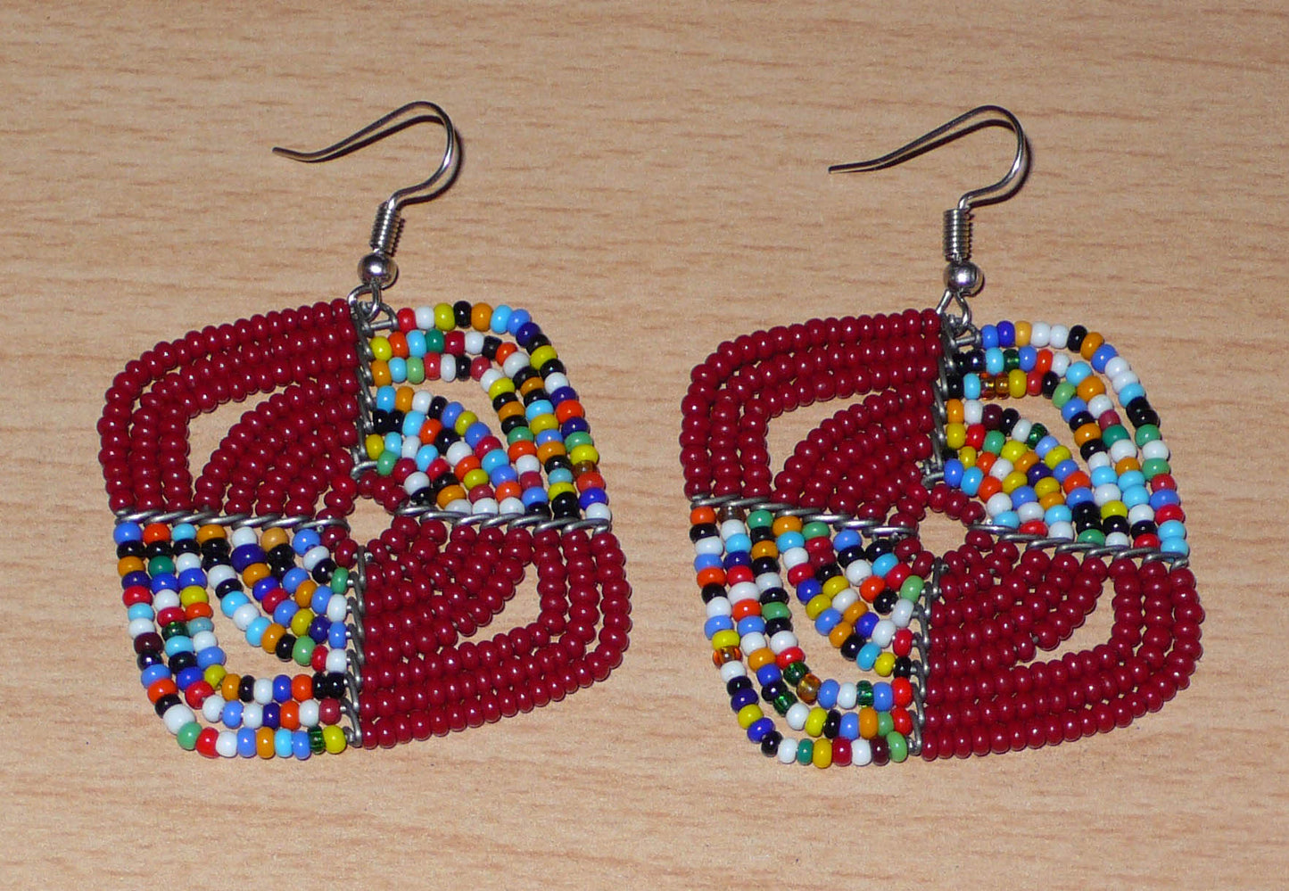 Boucles d'oreilles africaines Massai de confection artisanale kenyane : elles se composent de perles de rocaille bordeaux et d'un mélange de perles multicolores. Ces boucles d'oreilles aux accents afro bohème mesurent 6 cm de long et 4.5 cm de large, se portent avec des crochets en acier inoxydable sur des oreilles percées.