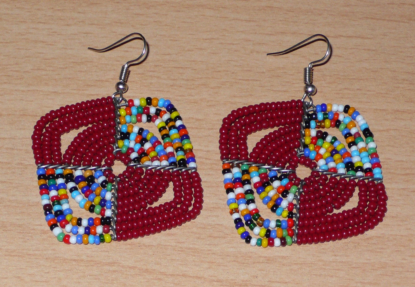 Boucles d'oreilles africaines Massai de confection artisanale kenyane : elles se composent de perles de rocaille bordeaux et d'un mélange de perles multicolores. Ces boucles d'oreilles aux accents afro bohème mesurent 6 cm de long et 4.5 cm de large, se portent avec des crochets en acier inoxydable sur des oreilles percées.