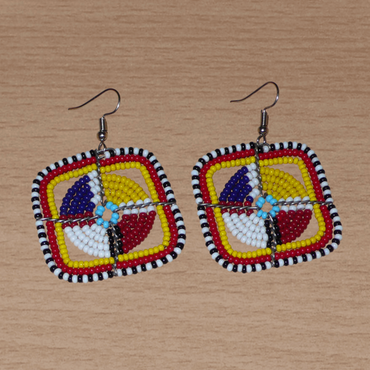 Boucles d'oreilles africaines de tradition ethnique Massai composées de perles de rocaille multicolores enfilées sur des structures géométriques en fils de fer. Ces boucles d'oreilles colorées aux accents exotiques mesurent 5.5 cm de long et 4.5 cm de large ; elles se portent avec des crochets en acier inoxydable sur des oreilles percées.