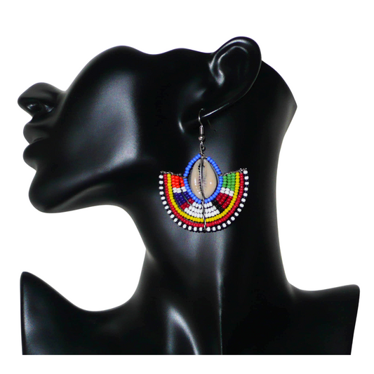 Apportez une touche ethnique à votre look avec cette jolie paire de boucles d'oreilles africaines Massai issues de l'artisanat traditionnel kenyan. Ces boucles d'oreilles aux accents tribaux sont composées de perles de rocaille bleues et multicolores et de coquillages cauris. De taille moyenne, elles mesurent 6 cm de long et 4.5 cm de large, et se portent avec des crochets en acier inoxydable sur des oreilles percées.