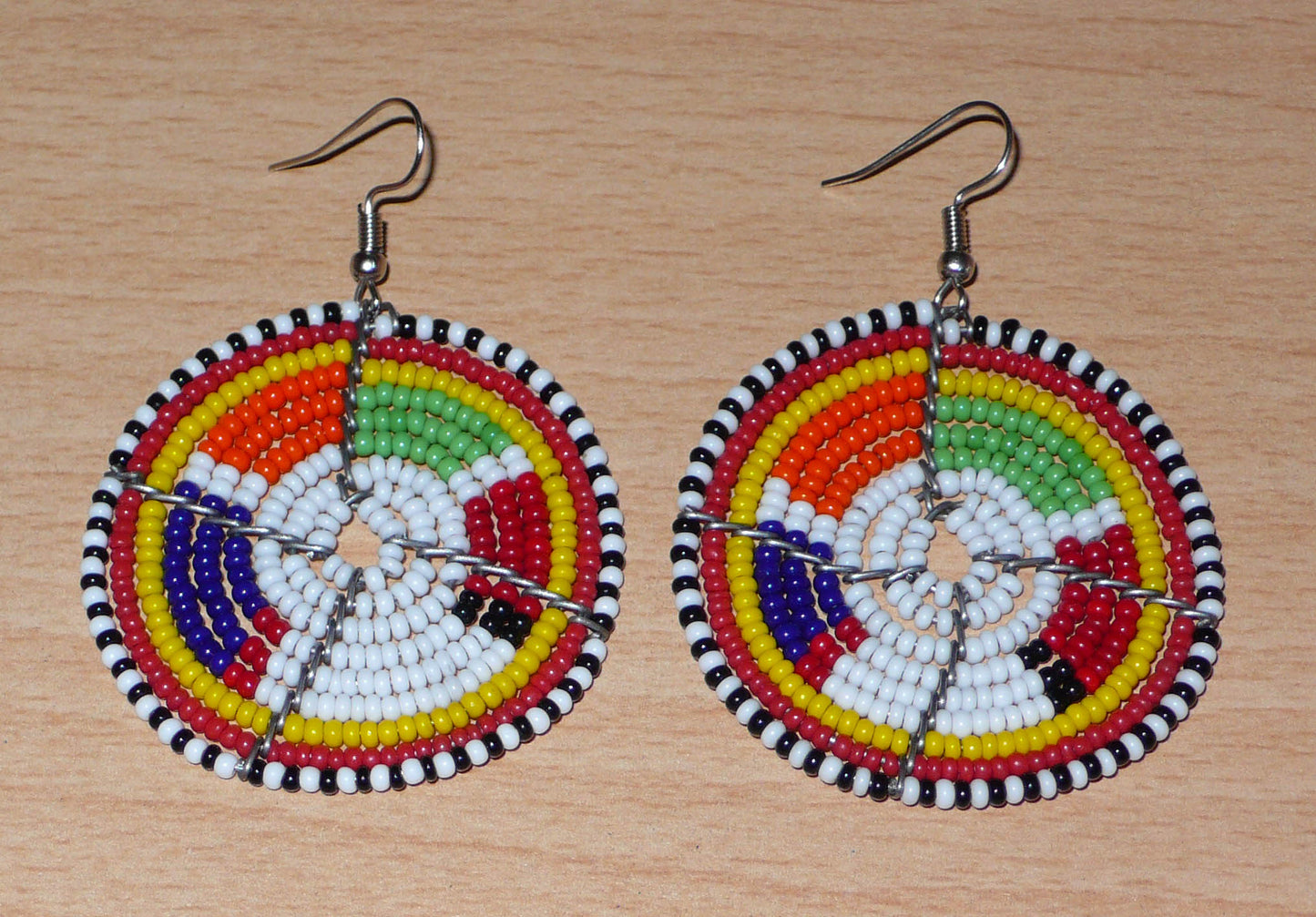 Boucles d'oreilles africaines de tradition tribale Massai composées de perles de rocaille blanches et multicolores montées en forme de disques. Elles mesurent 6.5 cm de long et 4.5 cm de large et se portent sur des oreilles percées.