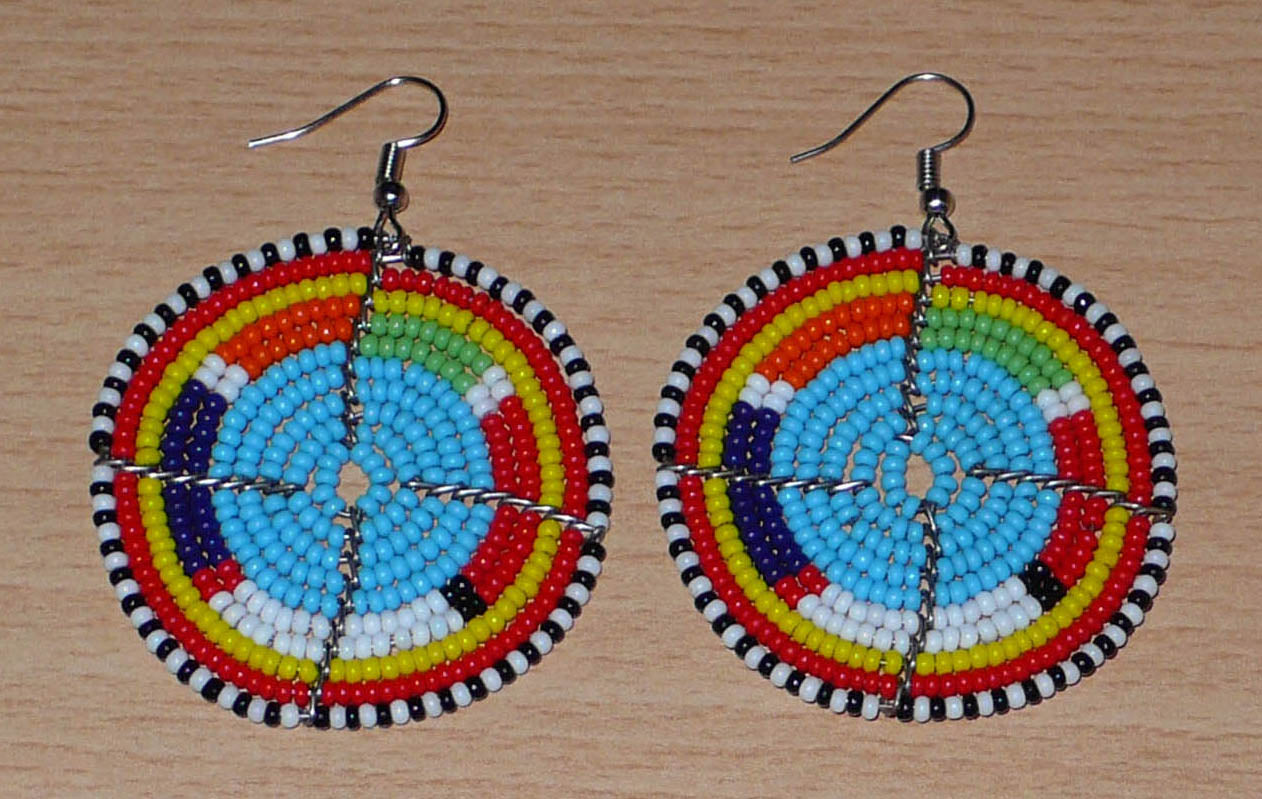 Boucles d'oreilles africaines rondes à motifs ethniques Massai composées de perles de rocaille bleues et multicolores. Elles mesurent 6.5 cm de long et 5 cm de large, et se portent sur des oreilles percées.