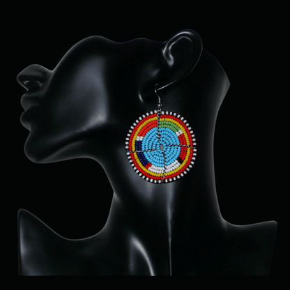 Boucles d'oreilles africaines rondes à motifs ethniques Massai composées de perles de rocaille bleues et multicolores. Elles mesurent 6.5 cm de long et 5 cm de large, et se portent sur des oreilles percées.