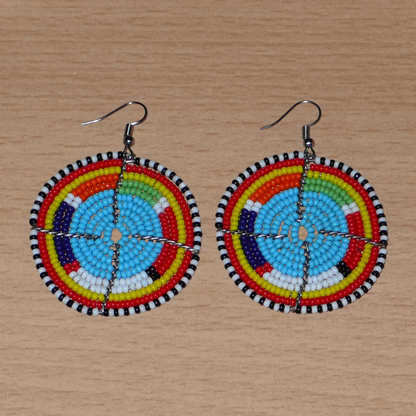 Boucles d'oreilles africaines rondes à motifs ethniques Massai composées de perles de rocaille bleues et multicolores. Elles mesurent 6.5 cm de long et 5 cm de large, et se portent sur des oreilles percées.