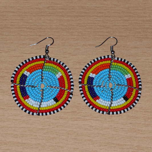 Boucles d'oreilles africaines rondes à motifs ethniques Massai composées de perles de rocaille bleues et multicolores. Elles mesurent 6.5 cm de long et 5 cm de large, et se portent sur des oreilles percées.