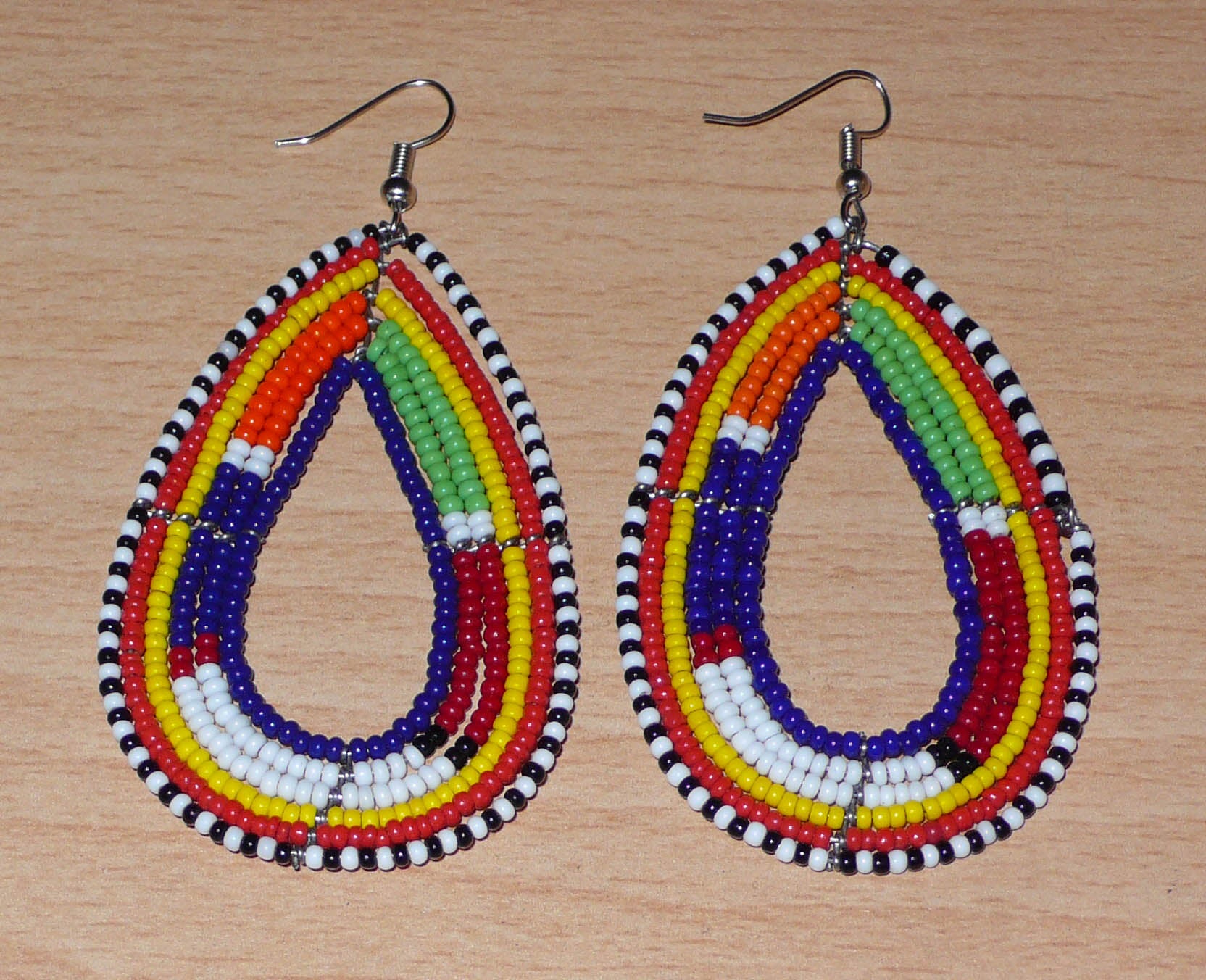 Apportez une touche ethnique à votre look avec ces longues boucles d'oreilles africaines traditionnelles aux couleurs et motifs tribaux Massai. Confectionnées selon la tradition artisanale kenyane, elles se composent de perles de rocaille bleu foncé et multicolores enfilées sur six rangées de fils de fer montés en forme de gouttes. Ces boucles d'oreilles mesurent 8.5 cm de long et 4 cm de large ; elles se portent avec des crochets en acier inoxydable sur des oreilles percées.