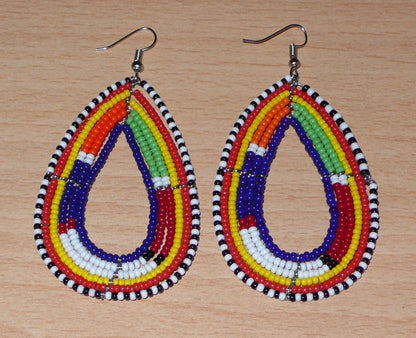 Apportez une touche ethnique à votre look avec ces longues boucles d'oreilles africaines traditionnelles aux couleurs et motifs tribaux Massai. Confectionnées selon la tradition artisanale kenyane, elles se composent de perles de rocaille bleu foncé et multicolores enfilées sur six rangées de fils de fer montés en forme de gouttes. Ces boucles d'oreilles mesurent 8.5 cm de long et 4 cm de large ; elles se portent avec des crochets en acier inoxydable sur des oreilles percées.