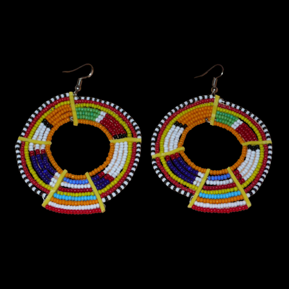 Boucles d'oreilles africaines tribales surdimensionnées, fabriquées au Kenya dans la plus pure tradition artisanale Massai. Elles se composent de perles de rocaille orange et multicolores tissées sur des structures circulaires en fils de fer fixés à des charnières en plastique jaune. Ces longues et larges boucles d'oreilles ethniques mesurent 8.5 cm de long et 6 cm de large ; elles se portent avec des crochets en acier inoxydable sur des oreilles percées.