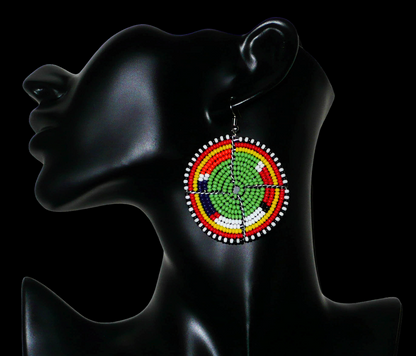 Boucles d'oreilles africaines Massai en perles de rocaille vertes et multicolores enfilées sur des structures circulaires en fils de fer. De taille moyenne, elles mesurent 6,5 cm de long et 4,5 cm de large ; elles se portent sur des oreilles percées.