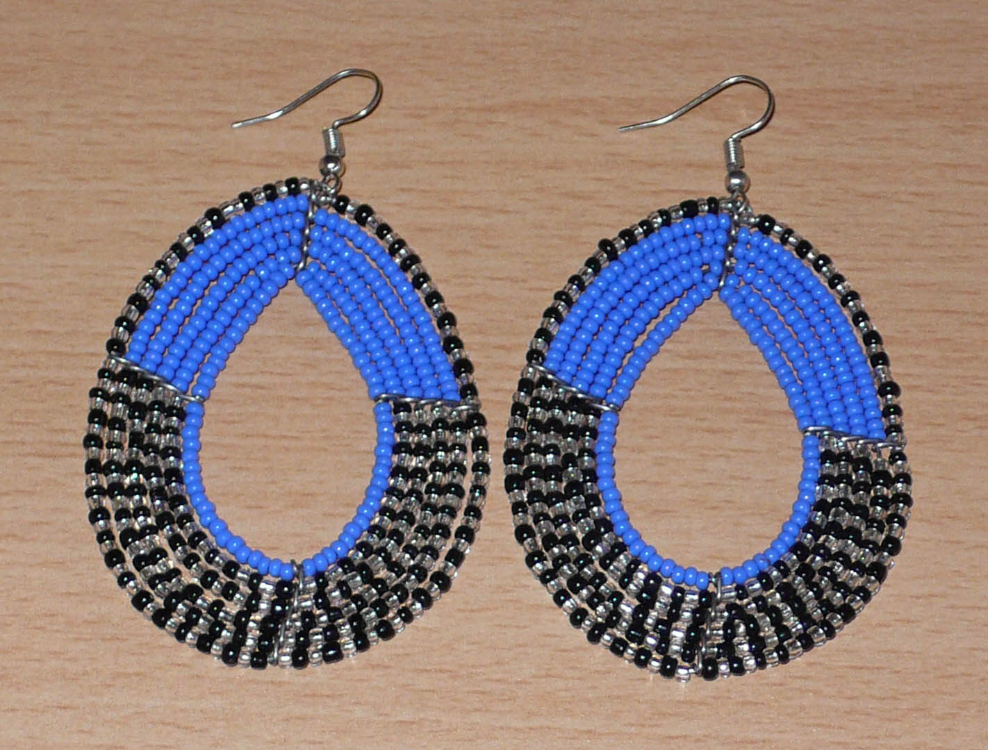 Longues boucles d'oreilles multi-rangs composées de perles de rocaille bleues, noires et gris nacré ; elles mesurent 8 cm de long et 5 cm de large et se portent avec des crochets sur des oreilles percées.