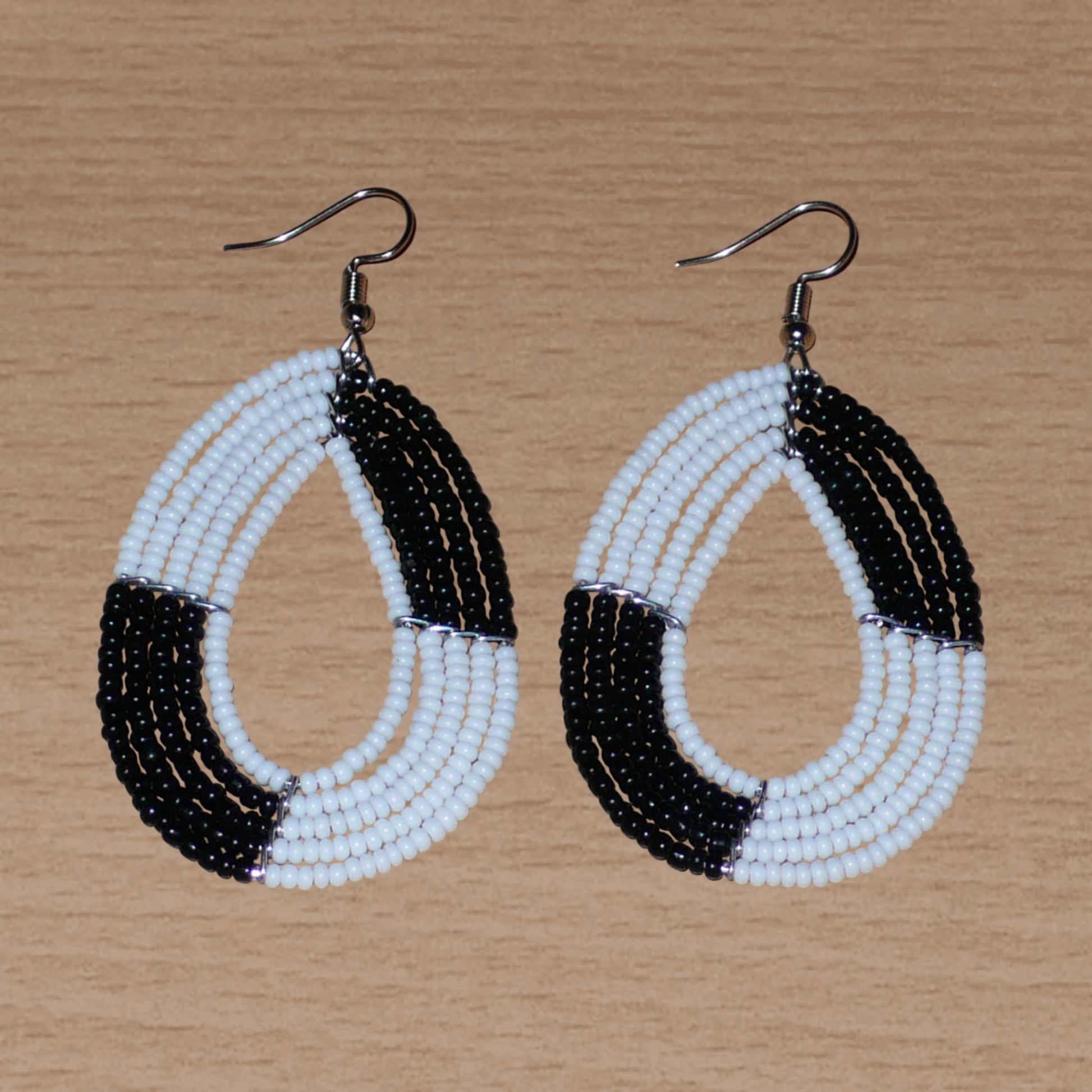 Boucles d'oreilles bicolores noires et blanches en forme de gouttes faites de perles de rocaille enfilées sur cinq rangées de fils. Elles mesurent 7,5 cm de long et 3 cm de large et se portent sur des oreilles percées.