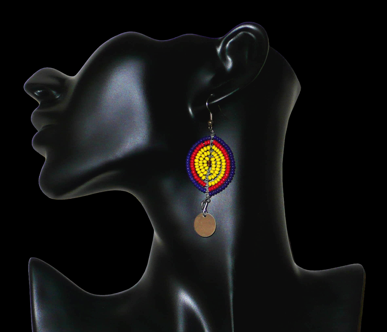 Boucles d'oreilles africaines en forme de boucliers Massai composées de perles de rocaille jaunes, rouges et bleu foncé ; elles se prolongent d'une petite pastille métallique. Ces boucles d'oreilles mesurent 7 cm de long et 2,5 cm de large ; elles se portent sur des oreilles percées. Timeless Fineries