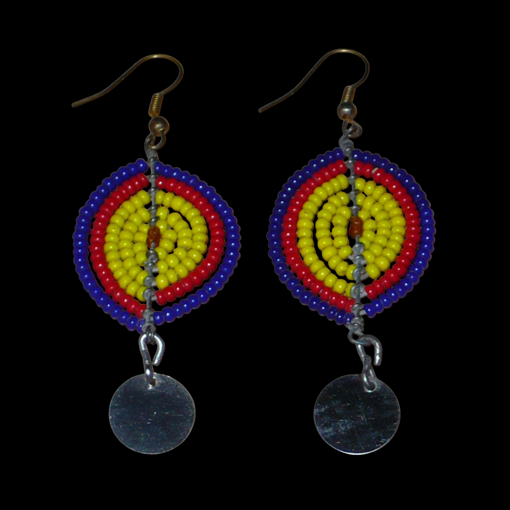 Boucles d'oreilles africaines en forme de boucliers Massai composées de perles de rocaille jaunes, rouges et bleu foncé ; elles se prolongent d'un disque métallique. Ces boucles d'oreilles mesurent 7 cm de long et 2,5 cm de large ; elles se portent sur des oreilles percées.