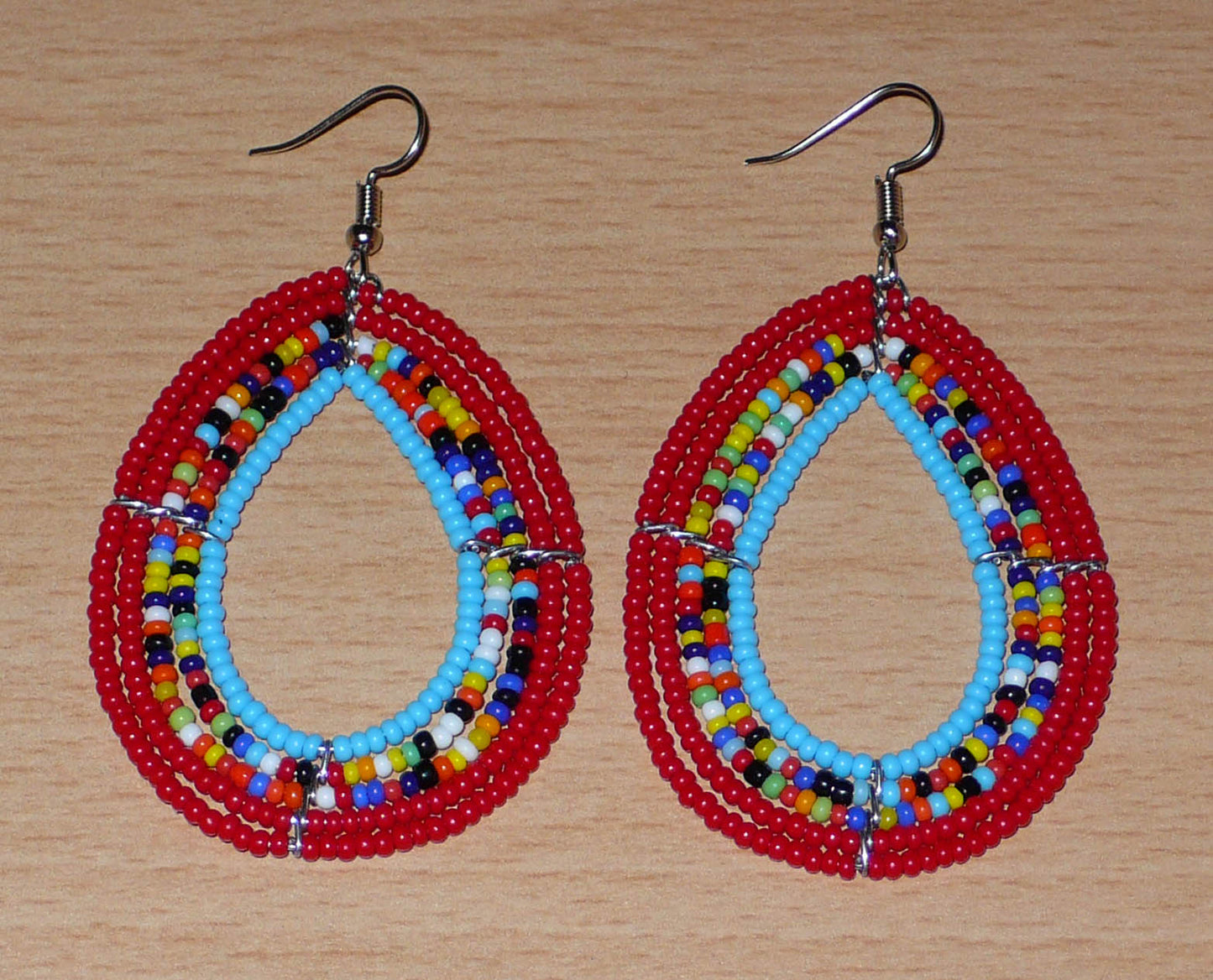 Boucles d'oreilles en forme de gouttes composées de perles de rocaille rouges, bleues et multicolores. Elles mesurent 7,5 cm de long et 4 cm de large et se portent sur des oreilles percées.