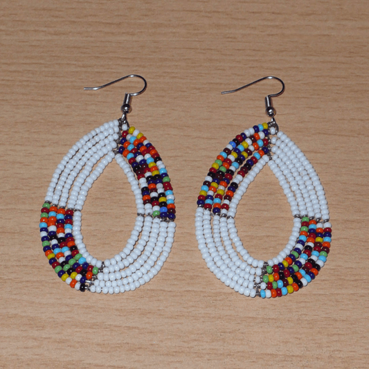 Boucles d'oreilles kenyanes en perles de rocaille blanches et multicolores enfilées sur plusieurs rangs de fils de fer montées en forme de gouttes ovales. De taille moyenne, ces boucles d'oreilles mesurent 7,5 cm de long et 4 cm de large, et se portent avec crochets en acier inoxydable sur des oreilles percées.